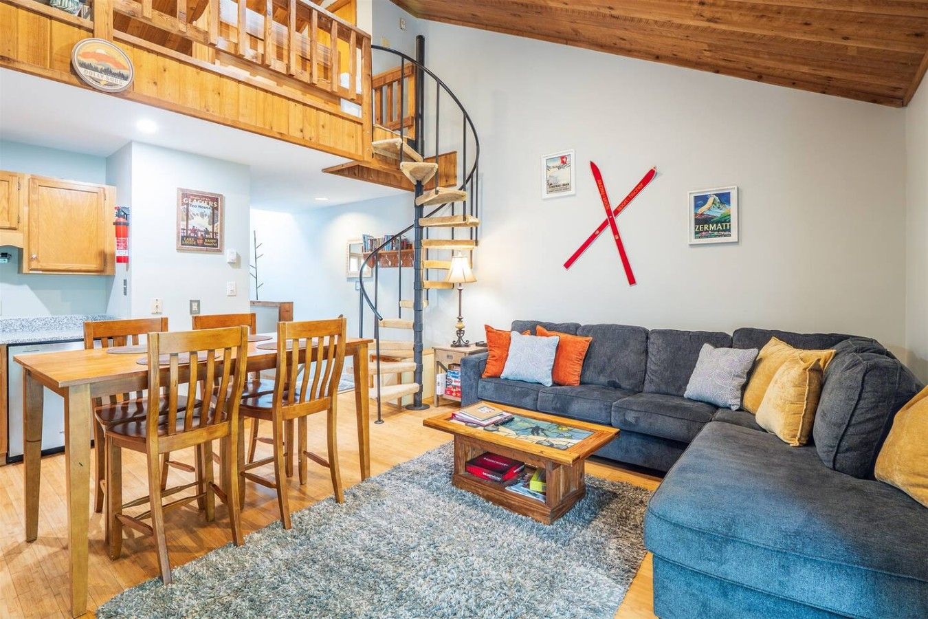 Una sala de estar con sofá, mesa de centro y sillas de madera. Se ve una escalera con barandilla de madera que conduce a un nivel superior.