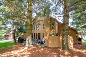 A two-story wooden cabin with a porch, surrounded by large trees.