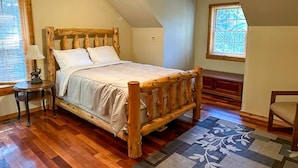A bedroom with a wooden bed, a nightstand, a lamp, a window, and a ceiling fan. - Back Country Cabin - Stunning, Secluded Property (Davis)