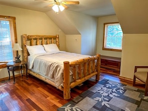 A bedroom with a wooden bed, a nightstand, a lamp, a window, and a ceiling fan.