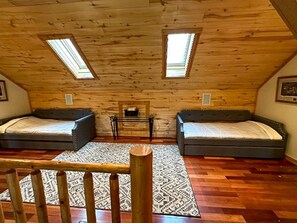 A loft bedroom with two beds, a small table, and a wooden floor.