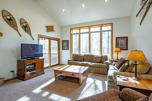 A spacious living room with a large window, a television, a sofa, a coffee table, and a lamp.