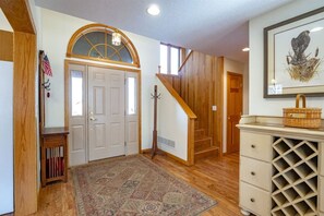 A wooden staircase leading to a second floor, a door with an arched window, and a framed artwork on the wall.