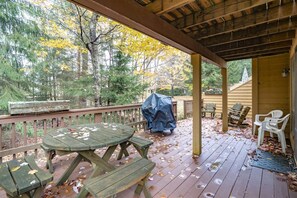 A covered outdoor deck with a picnic table and chairs, surrounded by trees and a wooden fence.