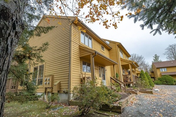A two-story wooden house with a porch, a small garden, and a gravel driveway.