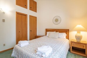 A bedroom with a bed, two wooden wardrobes, a bedside table with a lamp, and a decorative wall piece. - Deerfield Village 99 (Davis)