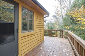 A wooden deck with a railing, a sliding glass door, and a view of trees with yellow leaves.