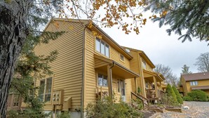 A two-story yellow house with a front porch, a visible chimney, and a small front yard with a tree and a garden bed. - Deerfield Village 099 (Davis)