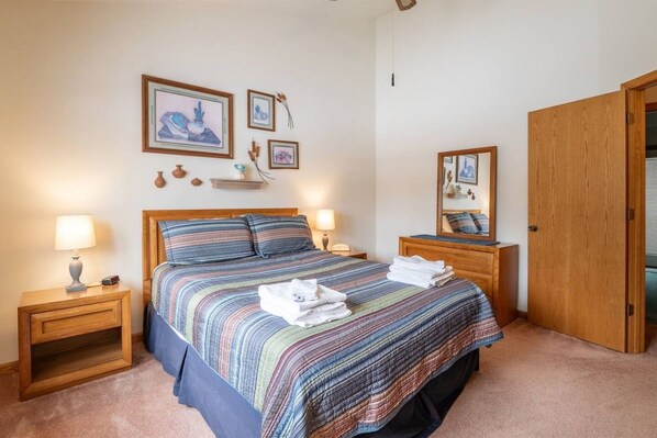 A bedroom with a bed, two bedside tables, a nightstand, a wooden wardrobe, and wall-mounted artwork.