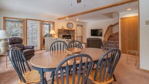 A dining area with a round table, chairs, a ceiling fan, a fireplace, and a TV. - Deerfield Village 099 (Davis)