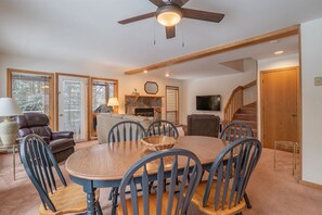 A dining area with a round table, chairs, a ceiling fan, a fireplace, and a TV.