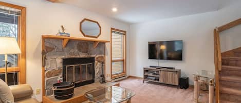 Una sala de estar con chimenea de piedra, un televisor de pantalla plana y una escalera.