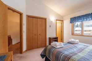 A bedroom with a bed, a wooden wardrobe, a chair, a small table, and a window with curtains.