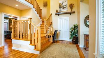 Un escalier en bois menant à un deuxième étage, une porte blanche, une plante en pot et une étagère avec des objets décoratifs.