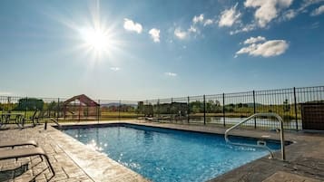 A swimming pool with a metal ladder, surrounded by a black fence, and a clear sky with the sun shining.