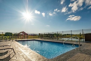 A swimming pool with a metal ladder, surrounded by a black fence, and a clear sky with the sun shining.