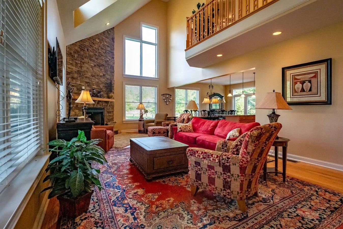 A spacious living room with a fireplace, a red sofa, patterned armchairs, and a large rug.