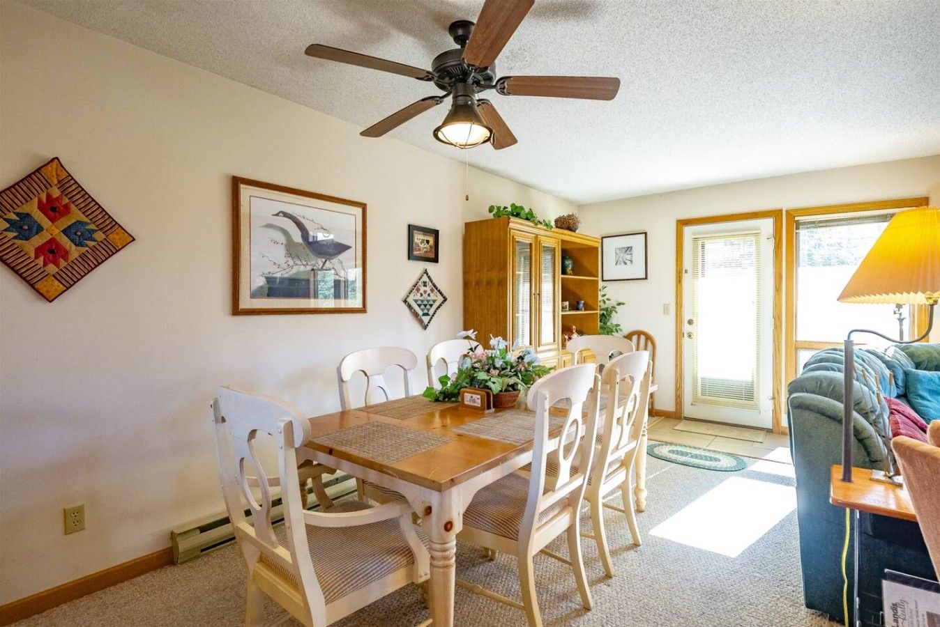A dining area with a wooden table, white chairs, a ceiling fan, and a bookshelf.