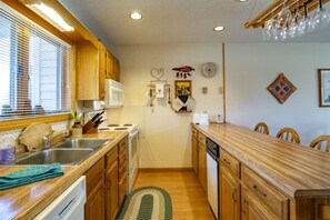 A compact kitchen with wooden cabinets, a microwave, a stove, and a sink. There is a green rug on the floor and a wooden dining table with chairs.