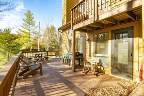 Eine Holzterrasse mit Picknicktischen und -stühlen, einem Grill und einem überdachten Bereich mit einer Tür.