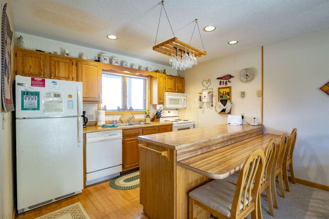 A compact kitchen with wooden cabinets, a built-in microwave, a refrigerator, and a dining area with wooden chairs.