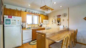 A compact kitchen with wooden cabinets, a built-in microwave, a refrigerator, and a dining area with wooden chairs.
