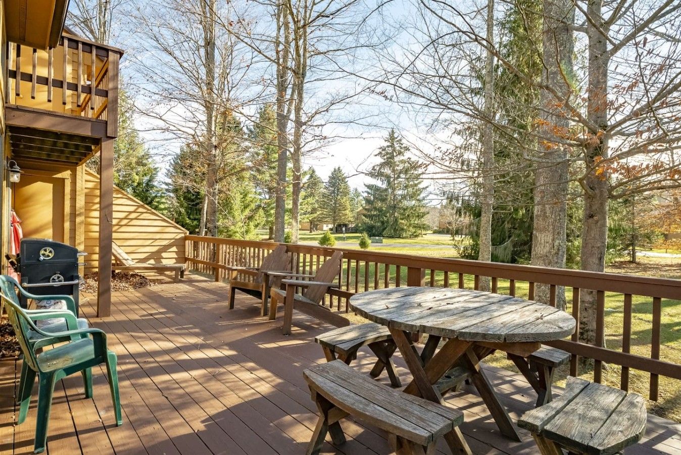 A wooden deck with picnic tables and chairs, overlooking a forested area.