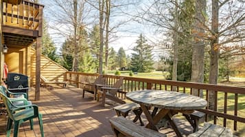 A wooden deck with picnic tables and chairs, overlooking a forested area.