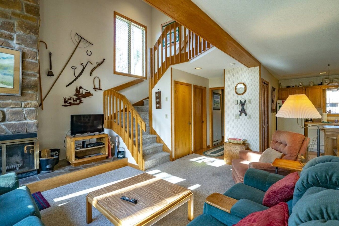 A cozy living room with a fireplace, a wooden staircase, and a kitchen area.