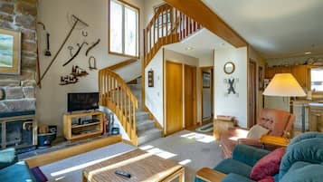 A cozy living room with a fireplace, a wooden staircase, and a kitchen area.