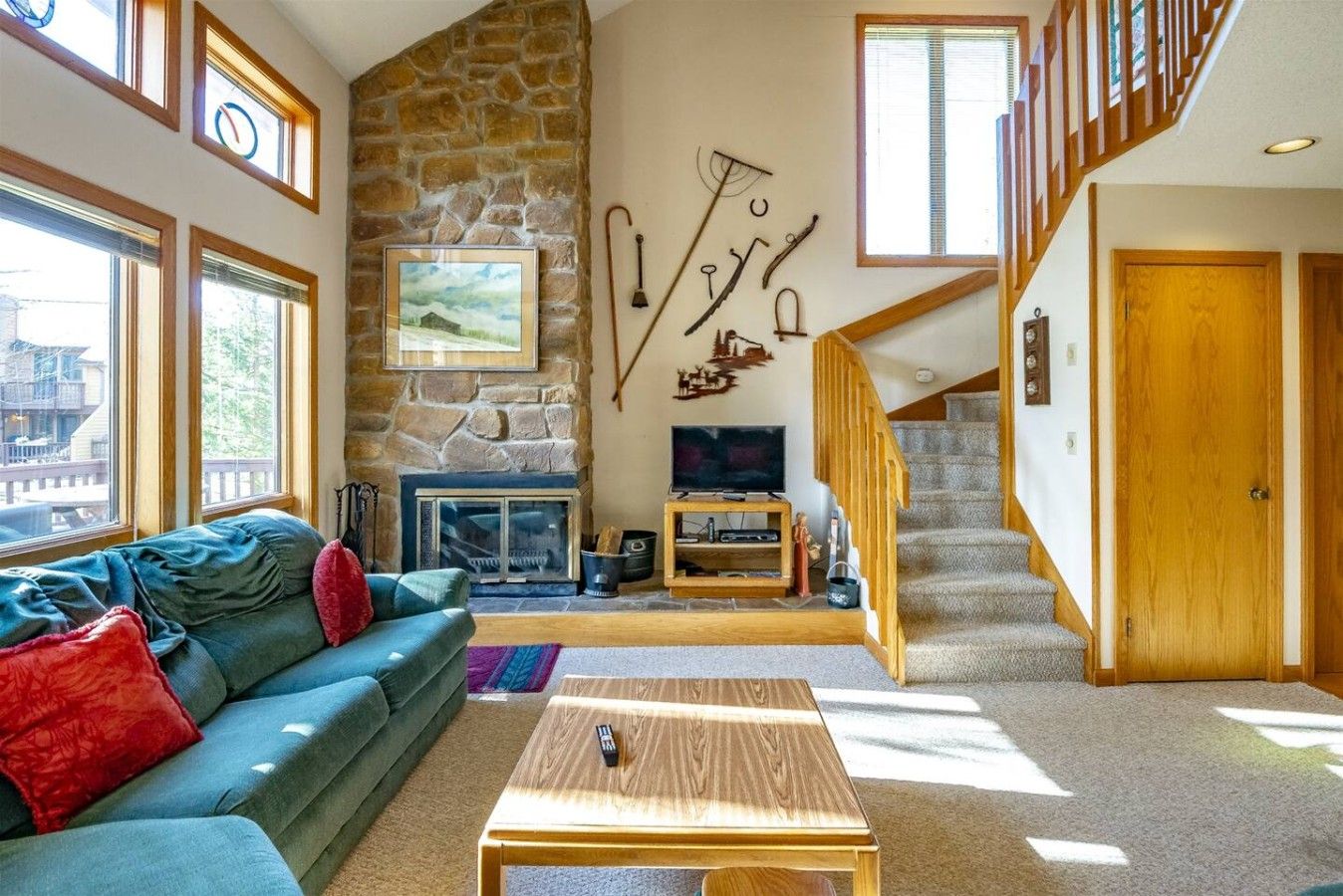 A living room with a stone fireplace, a television, a staircase, and a large window.