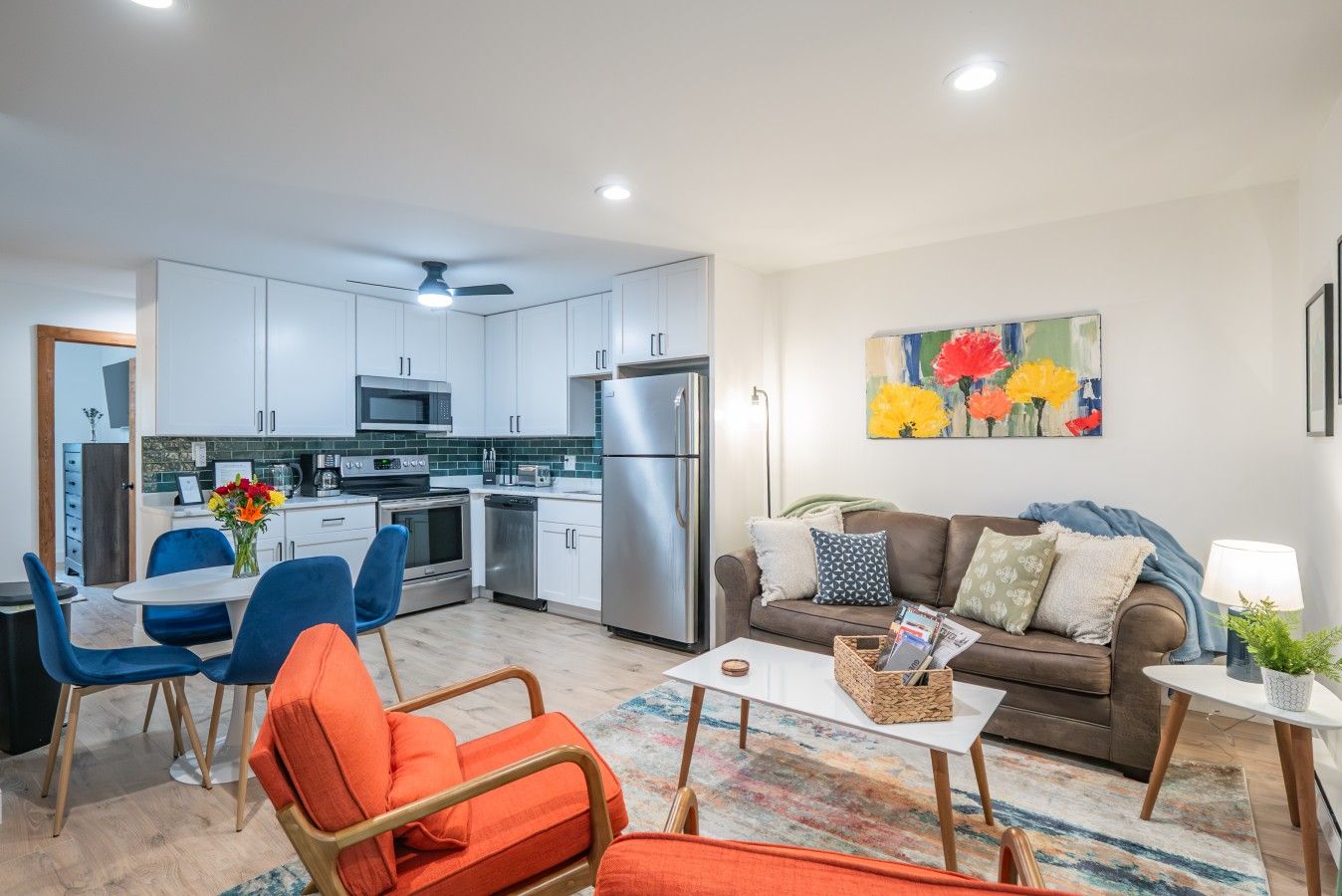 A modern kitchen with white cabinets, stainless steel appliances, and a dining area with blue chairs.