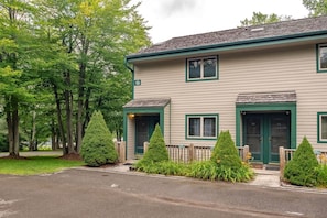 A two-story building with a green door and windows, a number 19 sign, and a paved driveway.