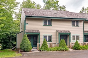 A two-story building with a numbered address sign, a front porch with a bench, and a small front yard with trimmed bushes.