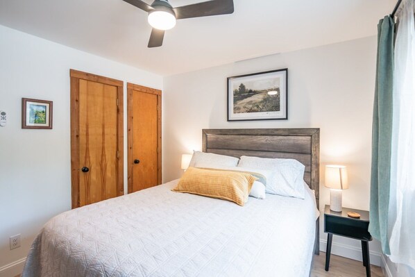 A bedroom with a bed, a bedside table with a lamp, a ceiling fan, and two wooden doors.