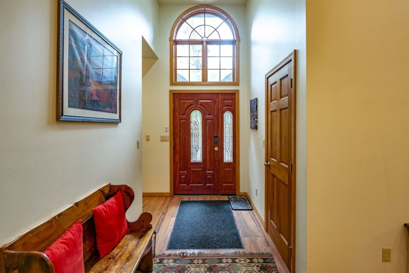 A hallway with a wooden bench, a door with glass panels, and a framed picture on the wall.