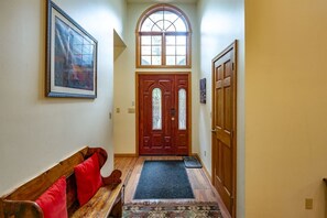 A hallway with a wooden bench, a door with glass panels, and a framed picture on the wall.