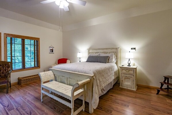 A bedroom with a bed, bedside tables, a chair, a window with blinds, and a ceiling fan.