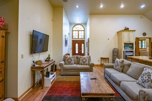 A living room with a TV, sofas, a coffee table, and a kitchen area with cabinets and appliances. - Family Escape w/ Hot Tub & Rec Room - Mtn Nights (Davis)