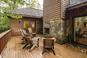 A wooden deck with Adirondack chairs and a stone fireplace.
