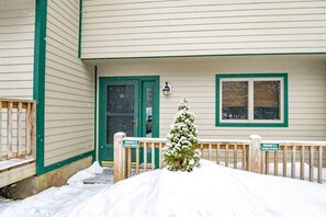 A building with a green door and windows, a small snow-covered tree, and a wooden fence with signs indicating parking restrictions.