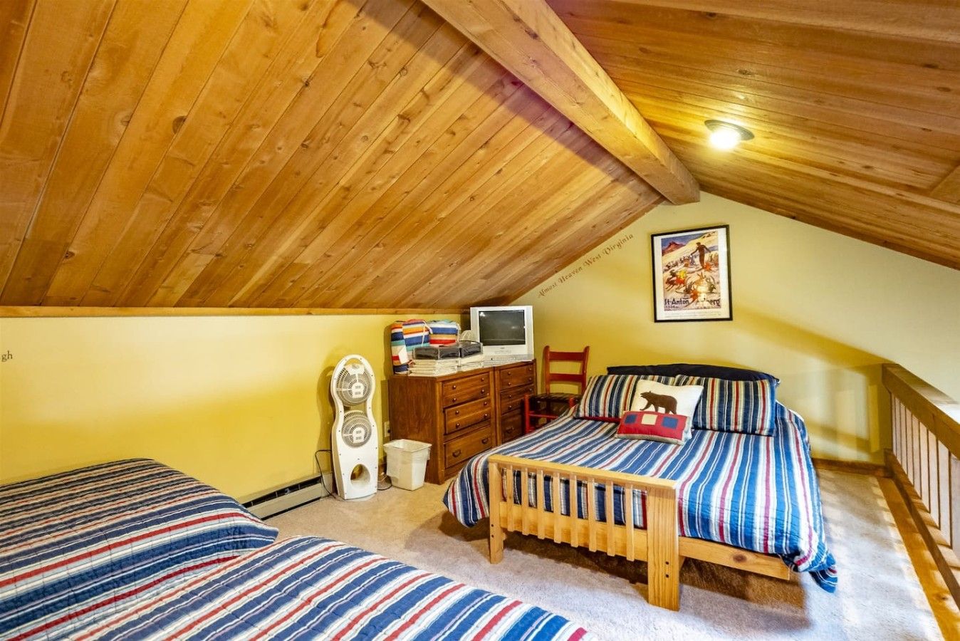 Une chambre avec deux lits, un plafond en bois, un bureau avec une télévision et une affiche accrochée au mur.
