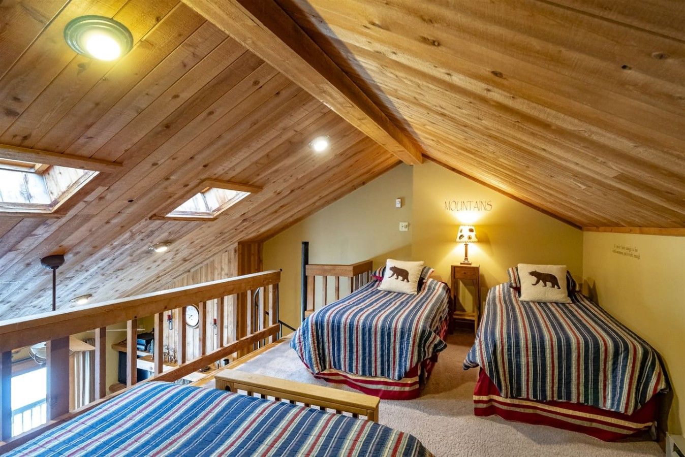 A cozy attic bedroom with two beds, a skylight, and a wooden railing.