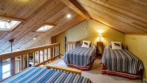 Une chambre mansardée chaleureuse avec deux lits, une lucarne et une rambarde en bois.