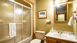 Une salle de bain avec une douche à parois de verre, des toilettes, un lavabo avec un miroir et un tableau encadré au mur.