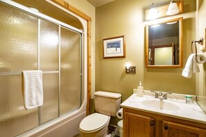 Un baño con cabina de ducha de vidrio, inodoro, lavamanos con espejo y un cuadro en la pared.