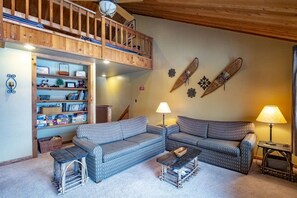 A cozy living room with a high wooden ceiling, a built-in bookshelf, two patterned sofas, a small wooden table, and a lamp. - Northwoods B5 - Ski-in/Ski-out at Timberline (Davis)