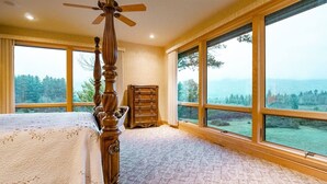 Un dormitorio con un ventanal grande, una cama de madera y un aparador.