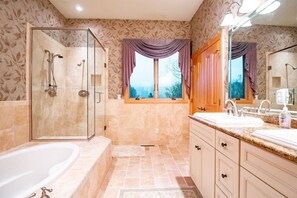 A bathroom with a glass-enclosed shower, a bathtub, a vanity with a sink, and a window with curtains.