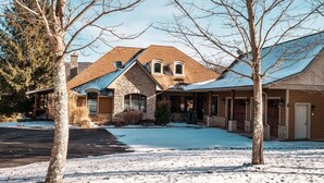 Una propiedad residencial con fachada de piedra, un porche cubierto y un camino de entrada cubierto de nieve.